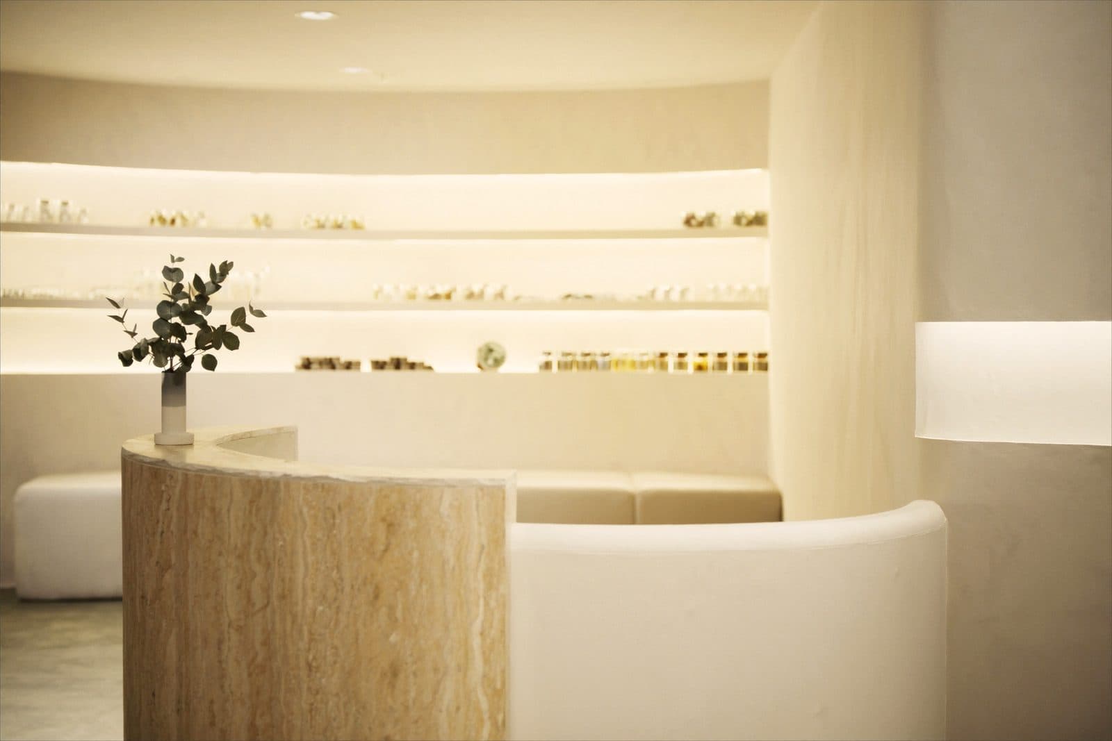 Elegant medspa reception lobby with travertine surfaces, curved seating and warm backlit shelving